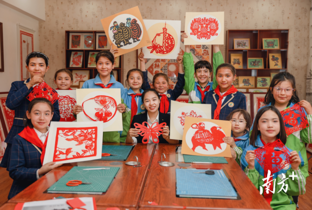 在明德小学非遗工作室内，广州市第四批“组团式”帮扶教师陆婉静与孩子们一起展示剪纸作品。