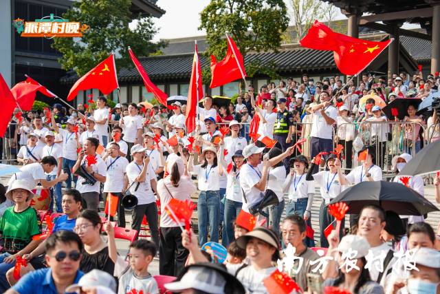 “村晚”现场旗帜高举，人山人海，非常热闹。 