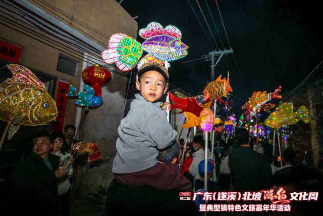 骑在爸爸肩上，手持小游鱼的小朋友。