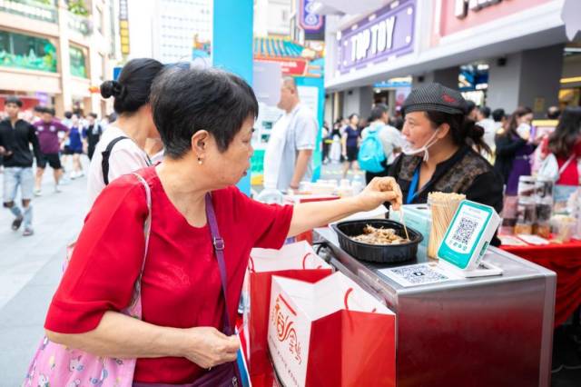 在驻河源市东源县仙塘镇帮镇扶村工作队展位前试吃手撕古法窑鸡的阿姨。