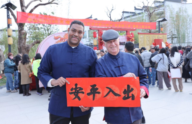 两位外国友人手持“出入平安”春联开心合影，感受中国传统年俗的独特魅力。