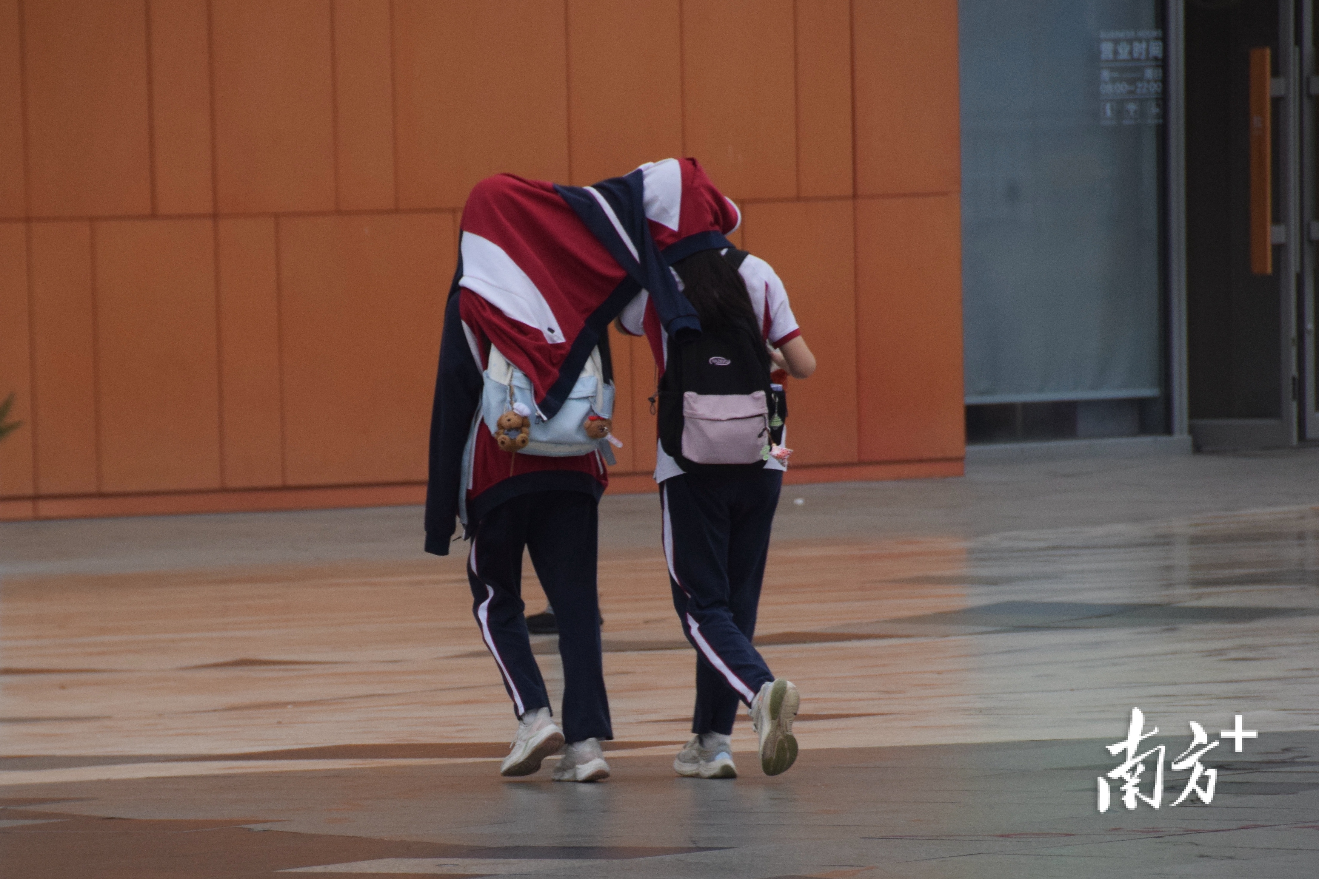 两名同学顶着衣服在雨中行走。 